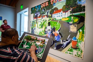 A member of the Arkansas Council of the Blind feels a touchable map representing Kerry James Marshall’s painting 
				entitled “Our Town,” which depicts an outdoor scene featuring two African American children running and bicycling towards the viewer.