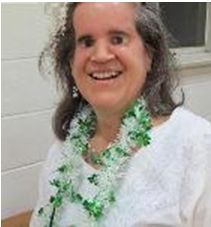 A color photo of Lisa.  She is smiling broadly and her dark hair is draped over her shoulders.  She wears a white blouse adorned with a lei of green and white blossoms hanging around her neck.